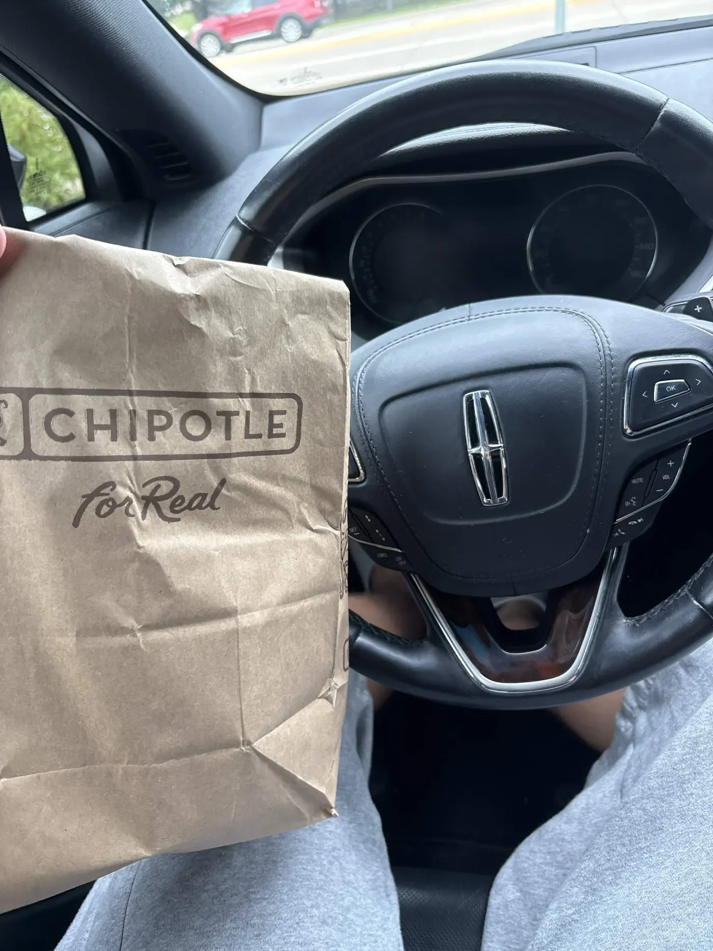 Chipotle takeout bag held in a car by the steering wheel