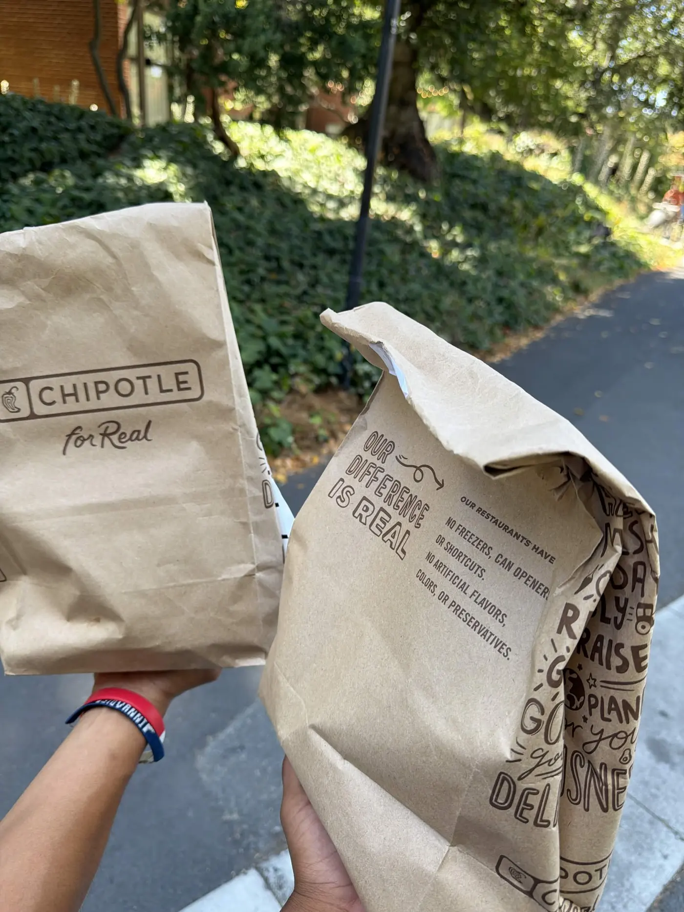 Two Chipotle bags held up outside on a sunny sidewalk