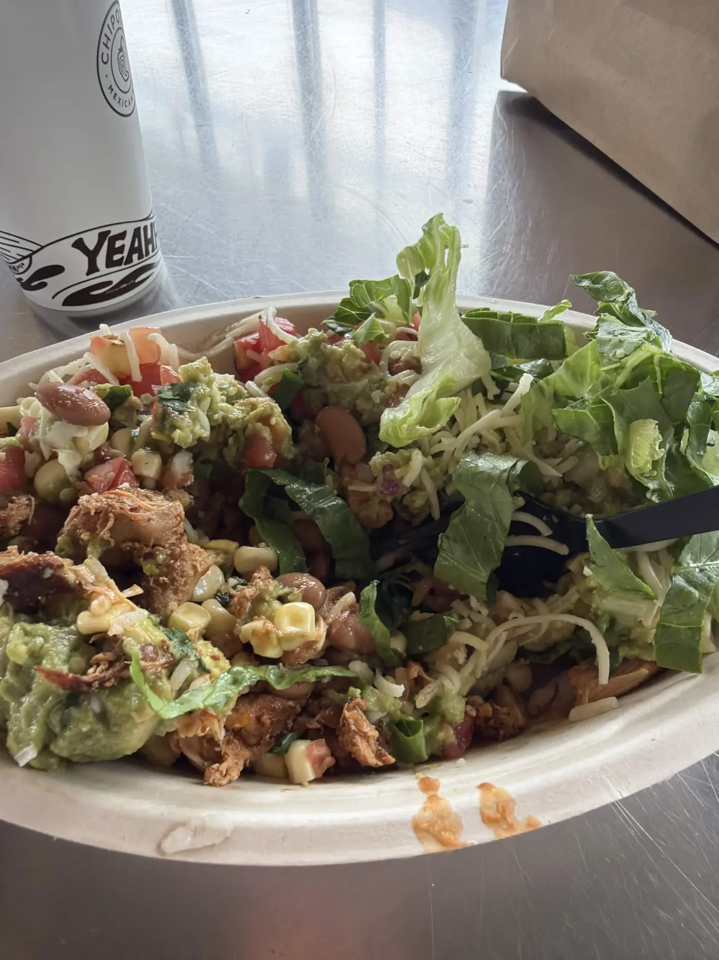 Chipotle bowl loaded with chicken, guacamole, corn and lettuce next to a Chipotle cup